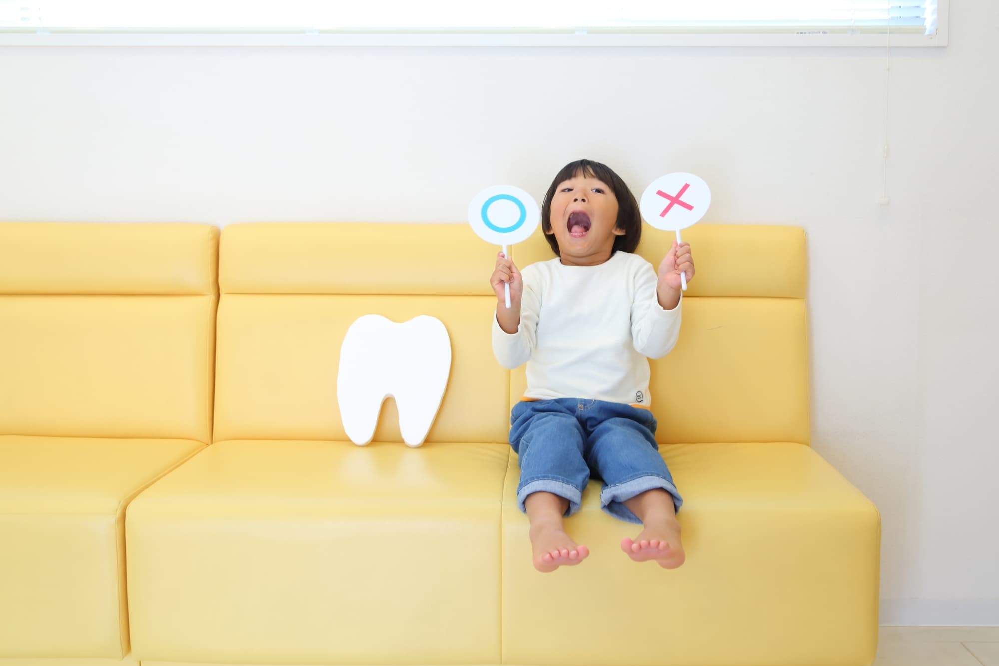 歯のモチーフと大きな口を開けるマルとバツの札を持つ子ども